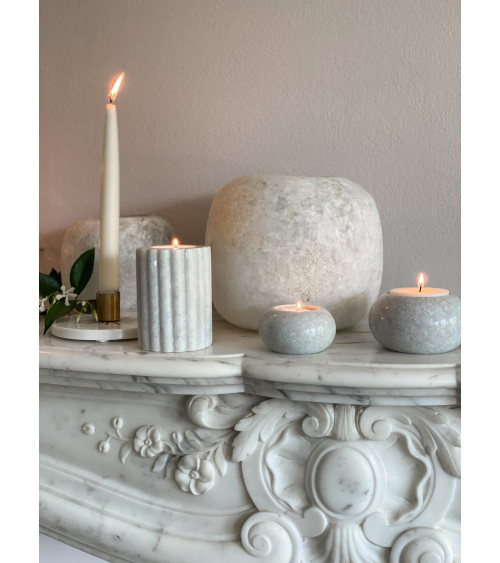 Le bougeoir en marbre blanc M placé sur une cheminée, entouré d’autres éléments décoratifs.