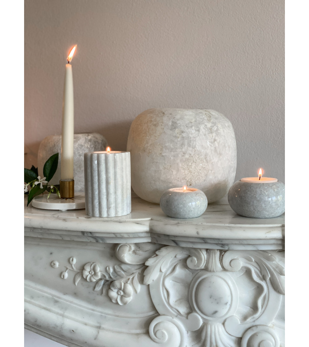 Le bougeoir en marbre blanc M placé sur une cheminée, entouré d’autres éléments décoratifs.