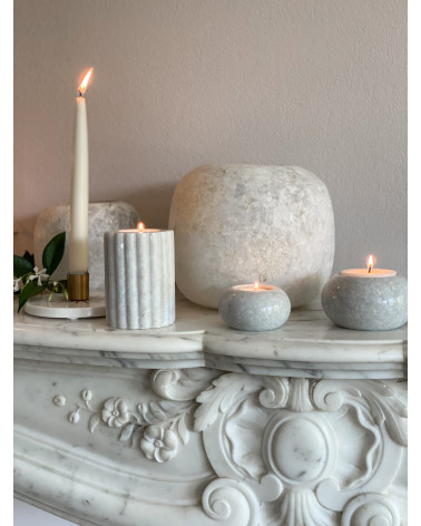 Le bougeoir en marbre blanc M placé sur une cheminée, entouré d’autres éléments décoratifs.