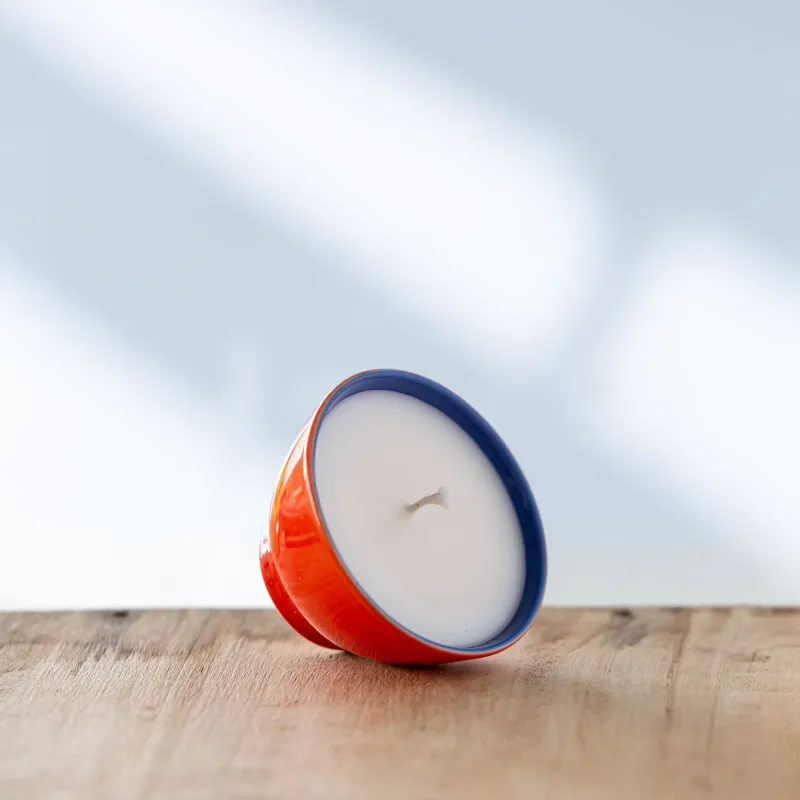 Bougie dans une tasse rouge et bleu posée de biais.