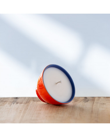 Bougie dans une tasse rouge et bleu posée de biais.