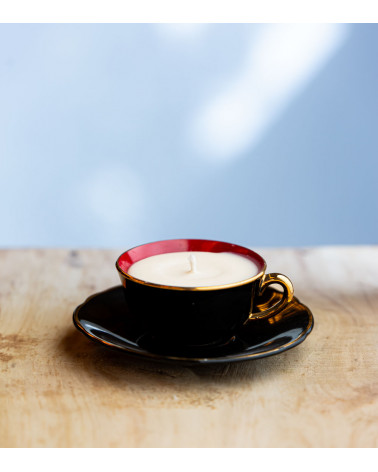 Bougie parfumée dans une élégante tasse à café noire avec intérieur rouge et bordure dorée.